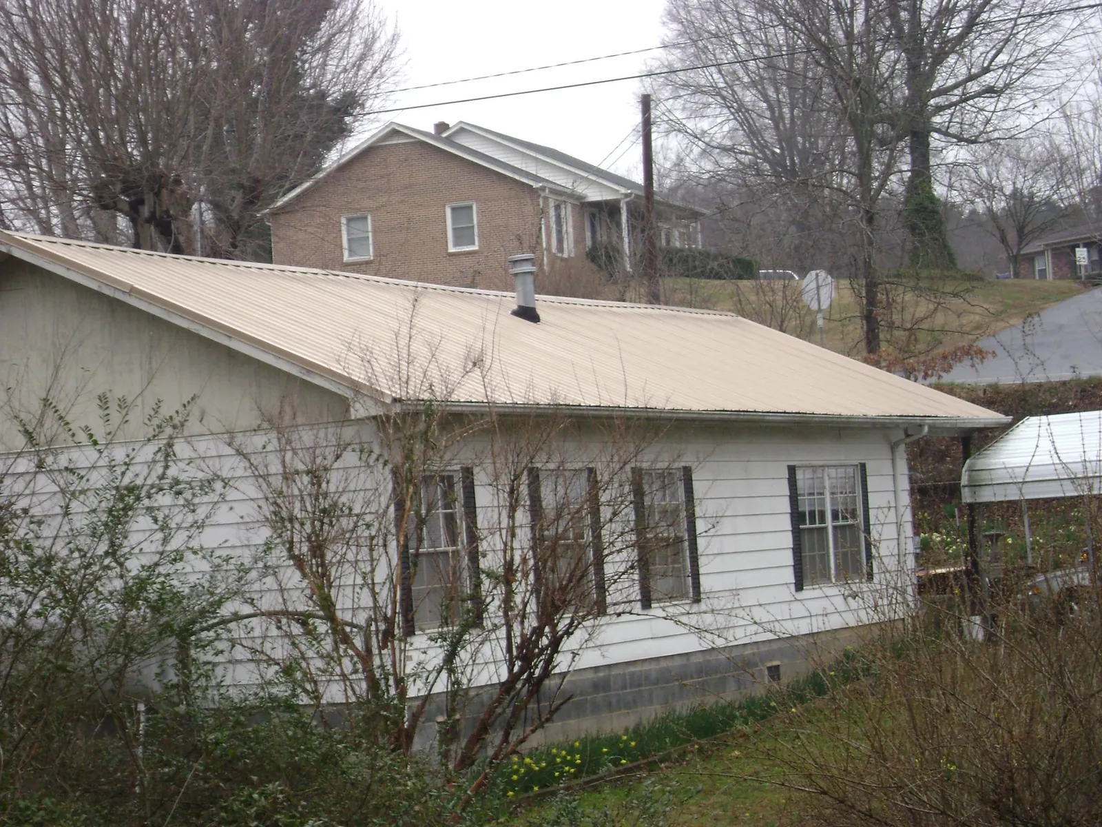 Tan metal roof on a white sided house set into a hillside — Commercial Roofing by Roofing Brothers in Westpoint